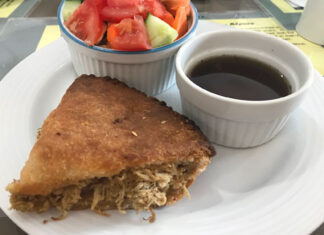 Acadian meat pie in Nova Scotia A triangular slice of Acadian meat pie with a side of beef jus and salad.
